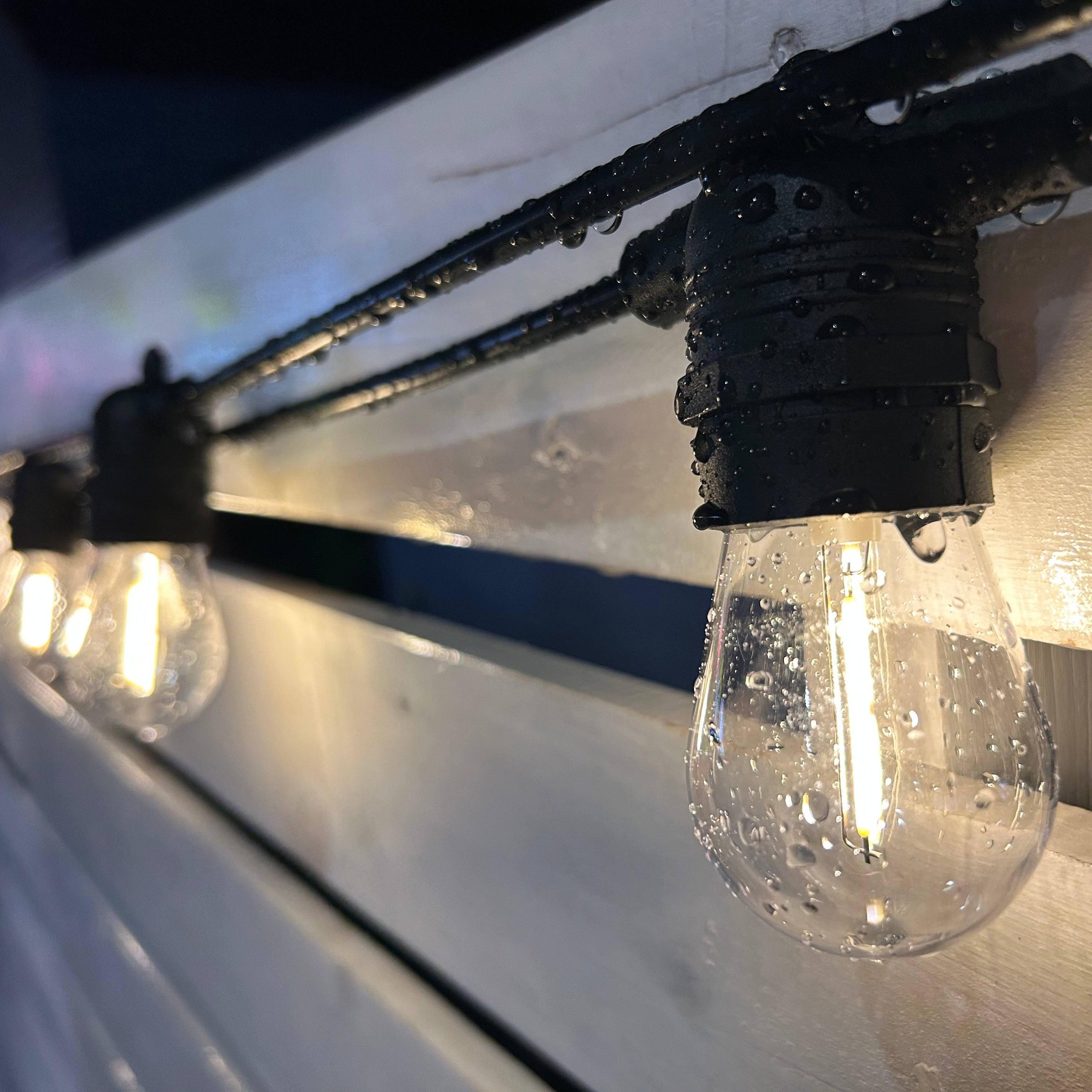 String of outdoor lights with clear bulbs hanging against a wooden surface.