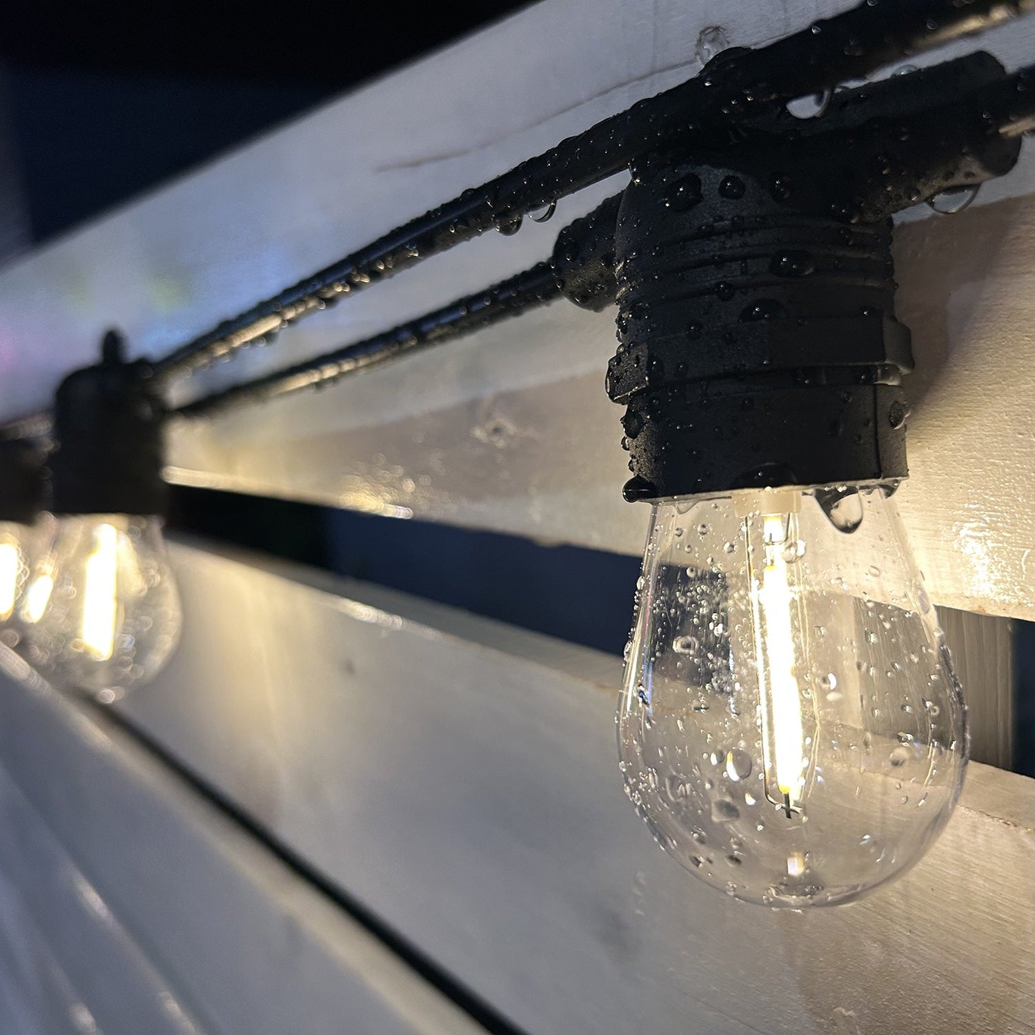 String of outdoor lights with clear bulbs and black wire on a white surface.