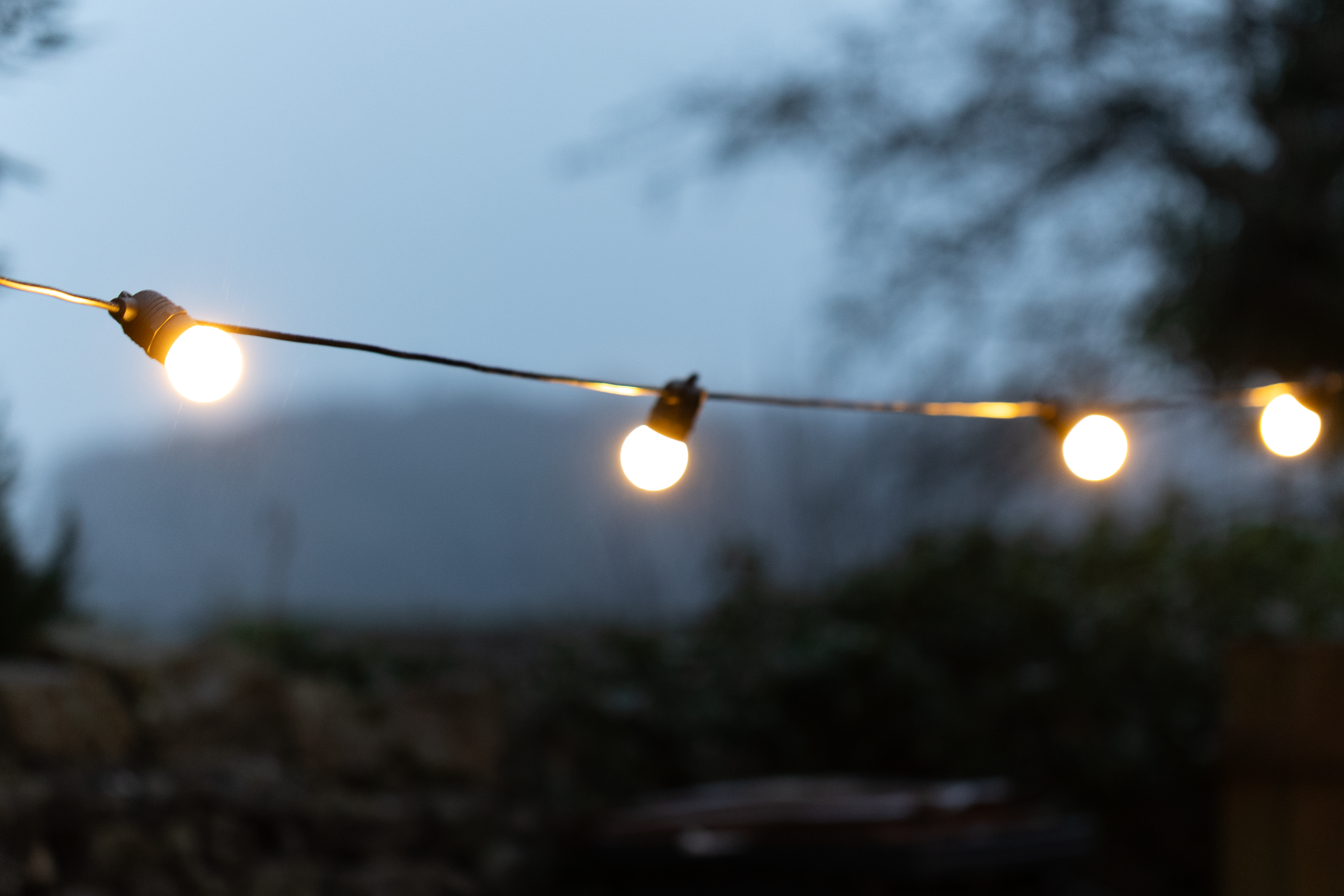 String lights with frosted bulbs on black rubber cable, illuminated and hanging on a wooden fence.